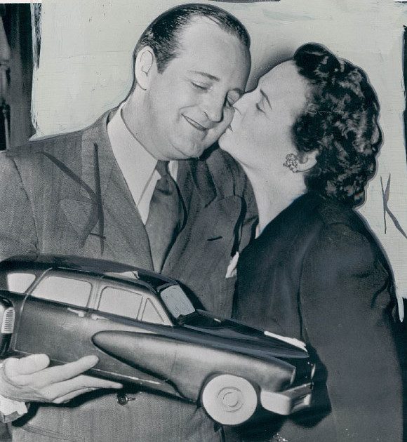 Preston Tucker, holding a model of the Tucker '48, kissed by his wife Vera